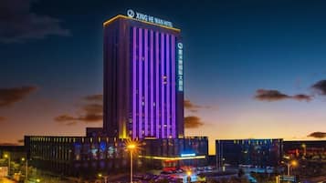 A tall hotel building with illuminated vertical lines, a parking lot, and street lights.