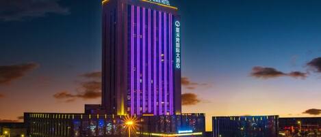 A tall hotel building with illuminated vertical lines, a parking lot, and street lights.