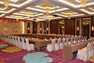 Un salón de conferencias con mesas y sillas largas, alfombra estampada y candelabro.