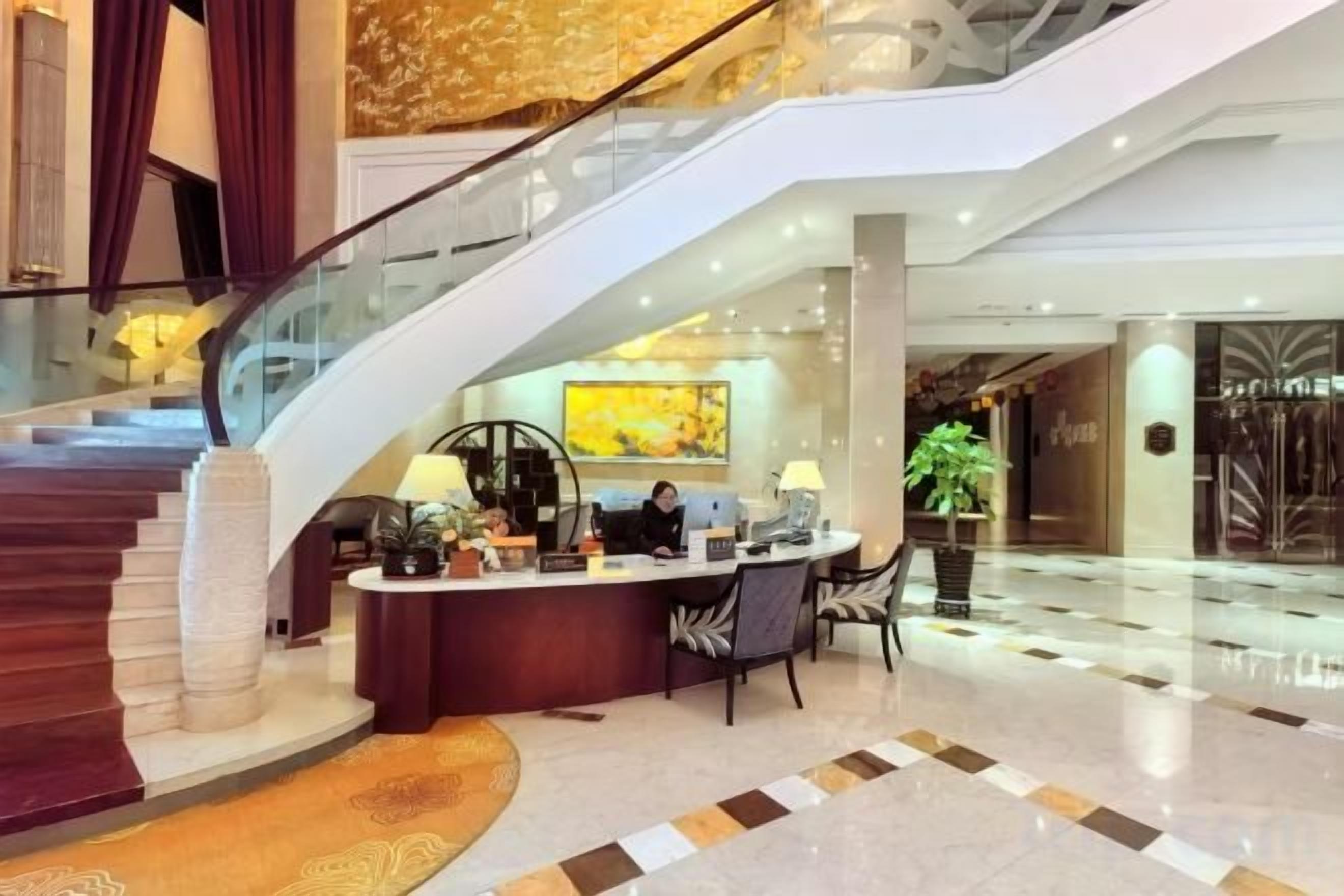 A hotel lobby with a reception desk, a staircase, and a large window.