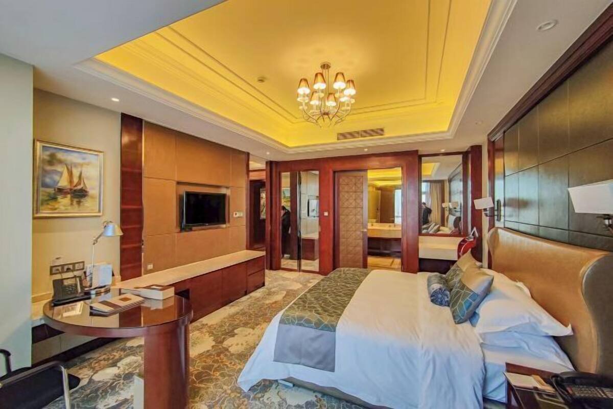 A hotel room with a bed, a desk, a TV, and a chandelier.