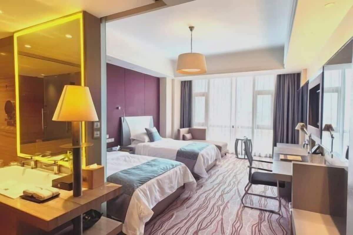 A hotel room with two beds, a desk, a chair, a large mirror, and a window with curtains.