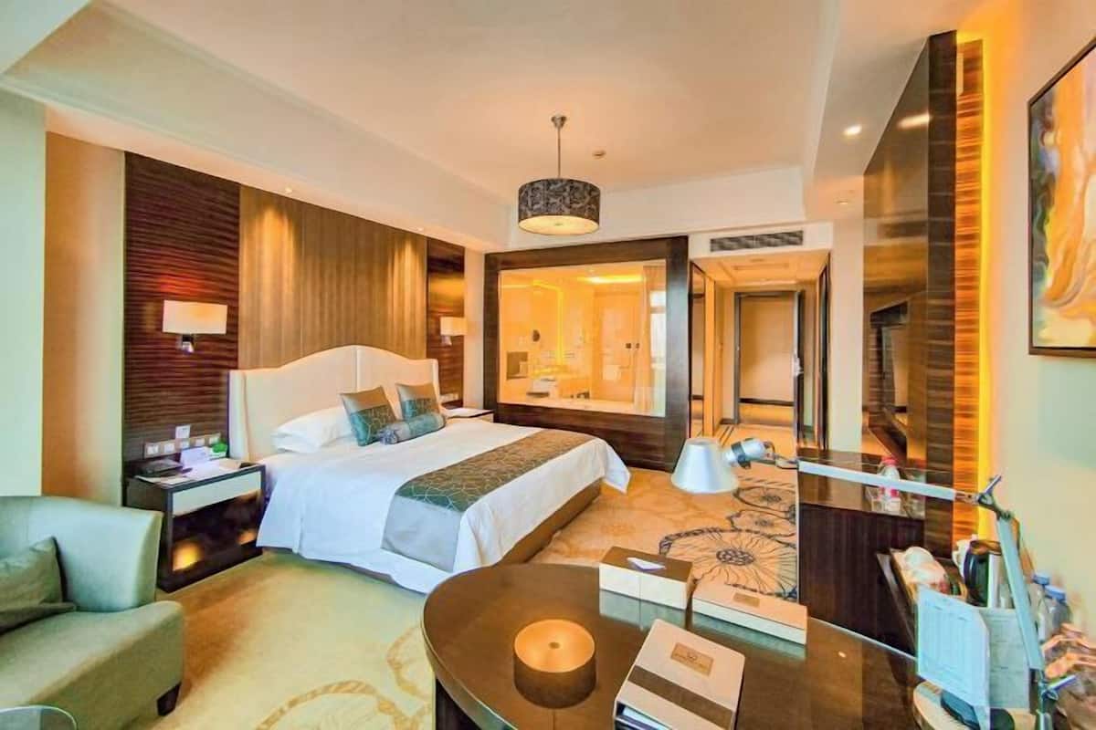 A hotel room with a large bed, bedside tables, a desk, a chair, a lamp, and a mirror.