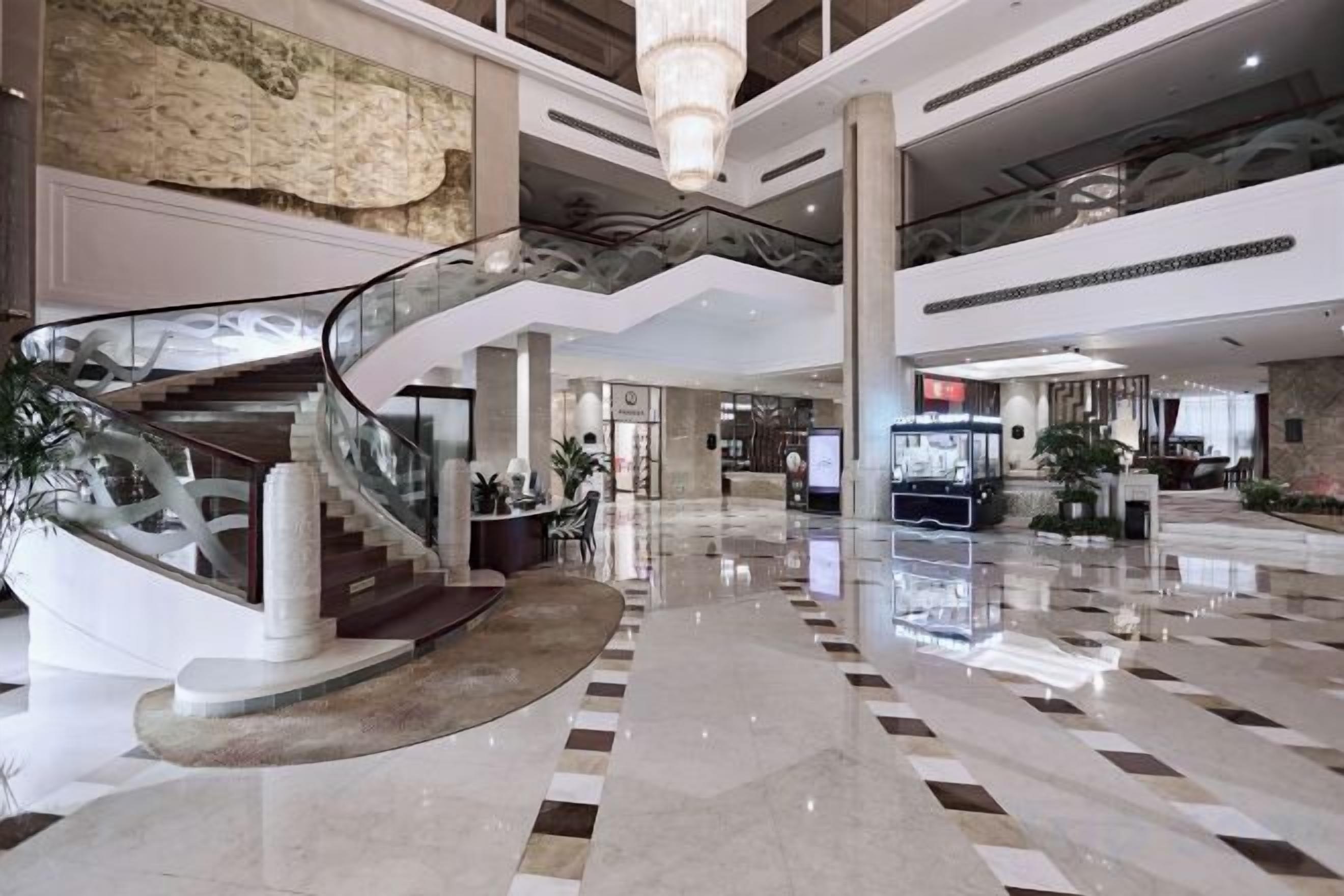 A spacious lobby with a central staircase, a reception desk, and a modern chandelier.