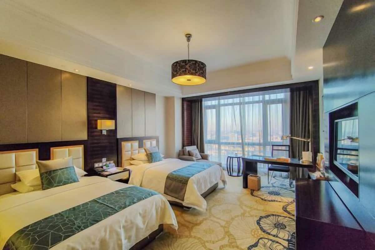 A hotel room with two beds, a desk, a TV, and a large window.