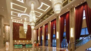 A spacious lobby with a grand staircase, large chandeliers, and a reception desk.