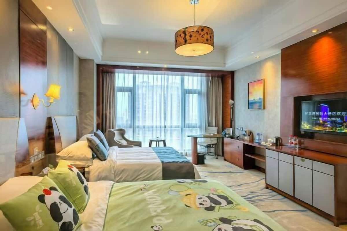 A hotel room with two beds, a desk, a television, and a large window.