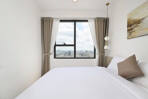 A hotel room with a bed, a window with curtains, a city view, and a painting on the wall. - Urban Zen Saigon - SOHO Residence D1 (Ho Chi Minh City)
