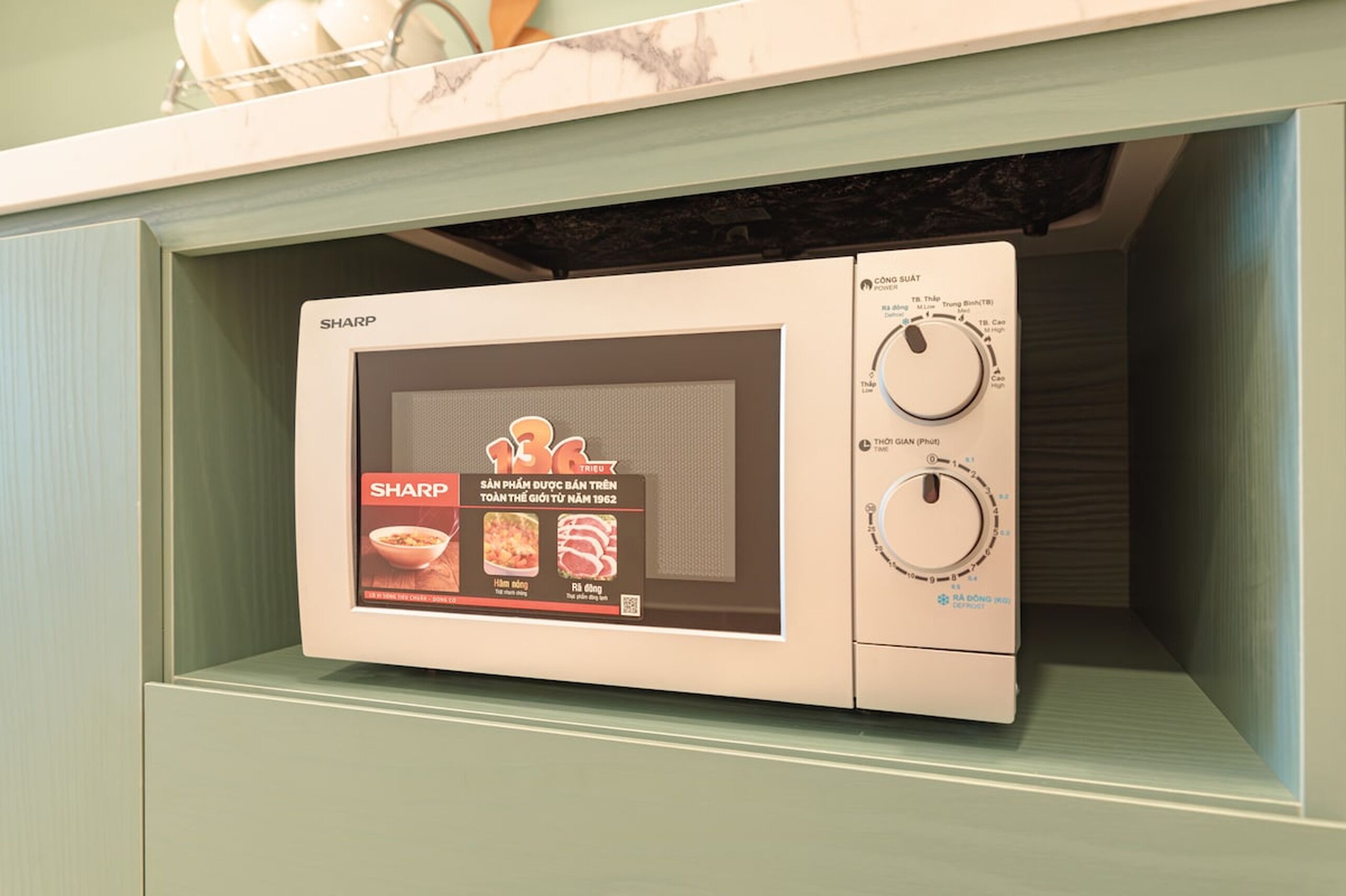A microwave with a digital display and two control knobs, placed inside a kitchen cabinet.