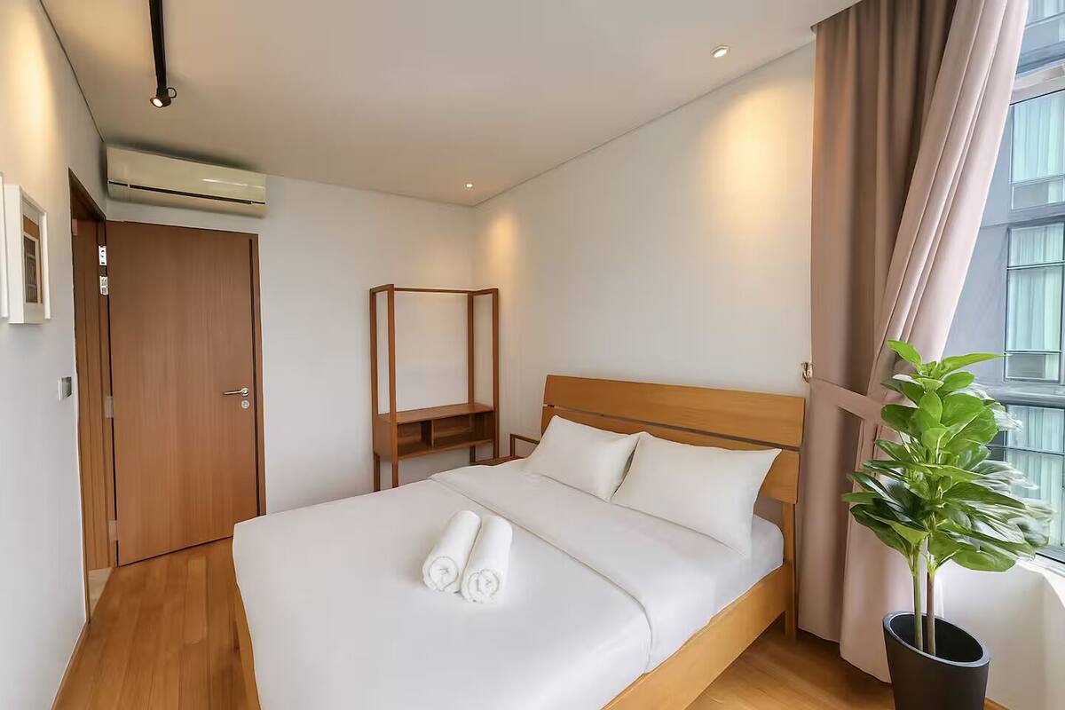 A hotel room with a wooden bed, a bedside table, a hanging chair, and a potted plant.