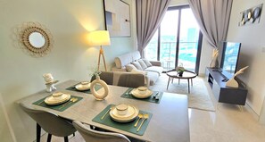 A dining area with a table set for four, a sofa, a TV, and a balcony with a view. - Urban Zen Saigon - SOHO Residence D1 (Ho Chi Minh City)