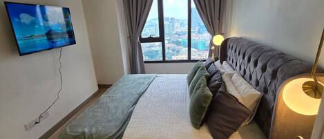 Un dormitorio con cama, televisor montado en la pared, ventana con vista a la ciudad y lámpara de noche.