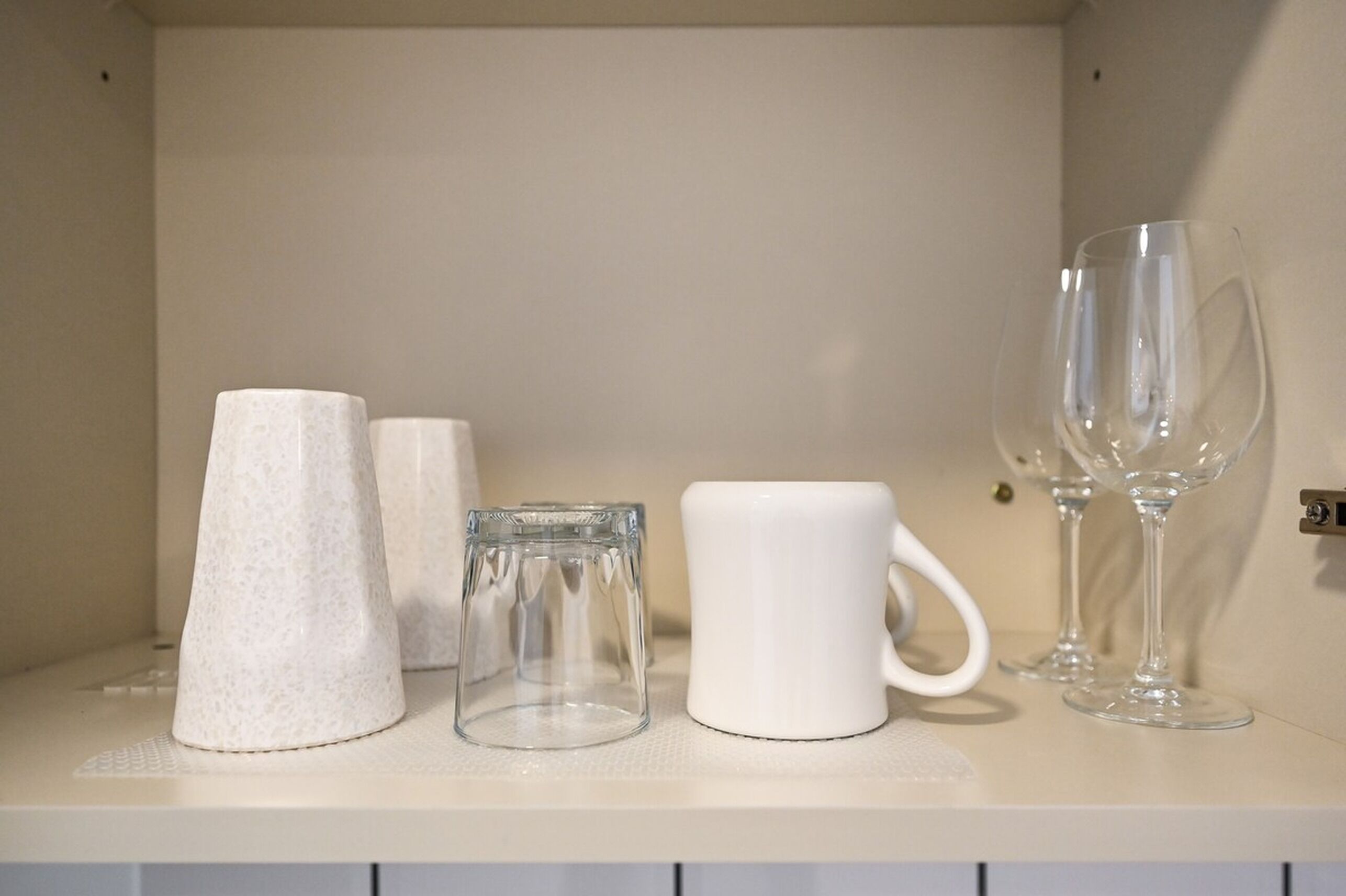 Una estantería con diversos vasos, incluyendo un vaso cónico, un vaso cilíndrico, una taza blanca y dos copas de vino.