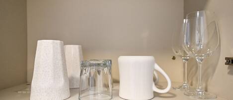 Una estantería con diversos vasos, incluyendo un vaso cónico, un vaso cilíndrico, una taza blanca y dos copas de vino.