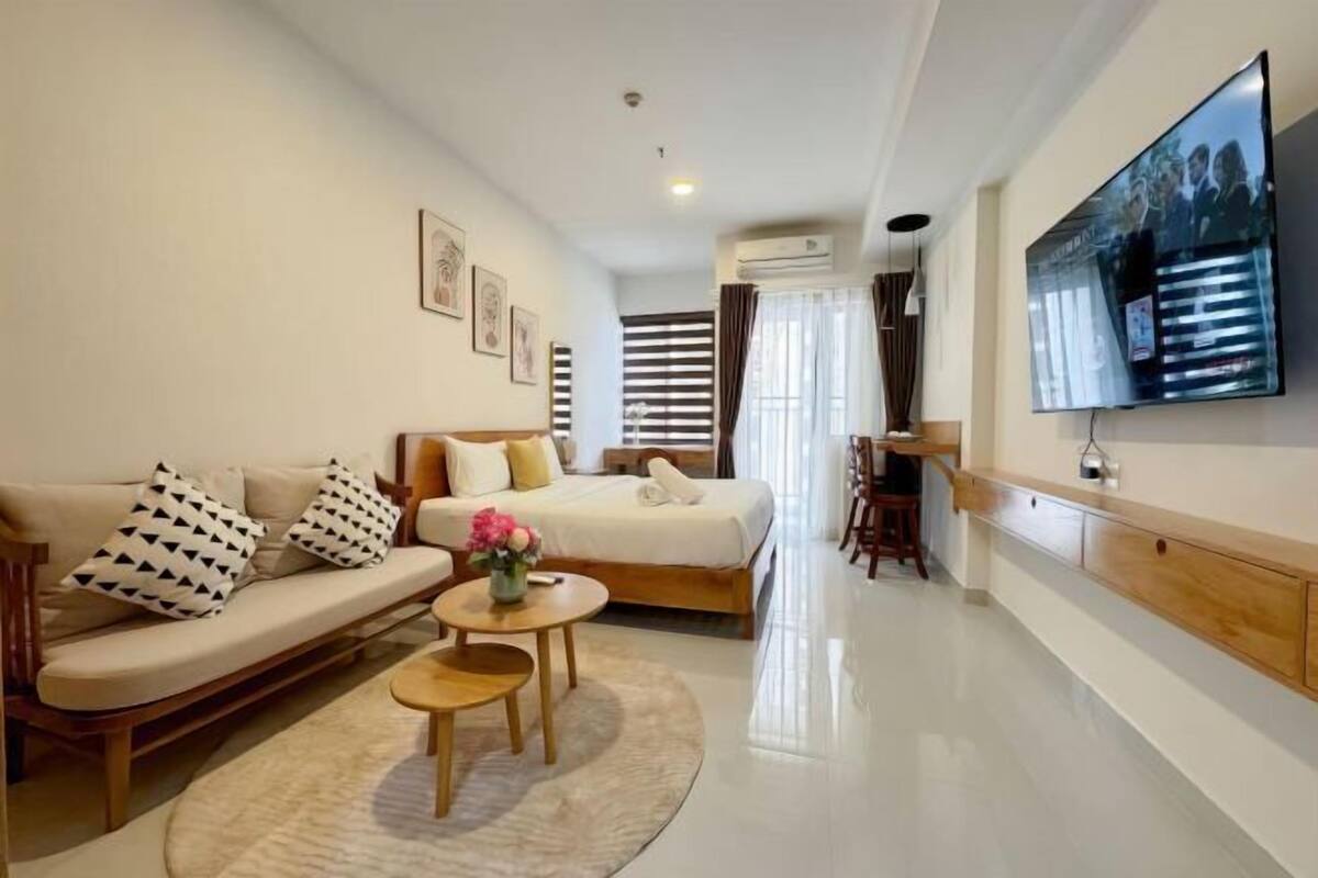 A modern hotel room with a sofa, a bed, a TV, and a small table with flowers.