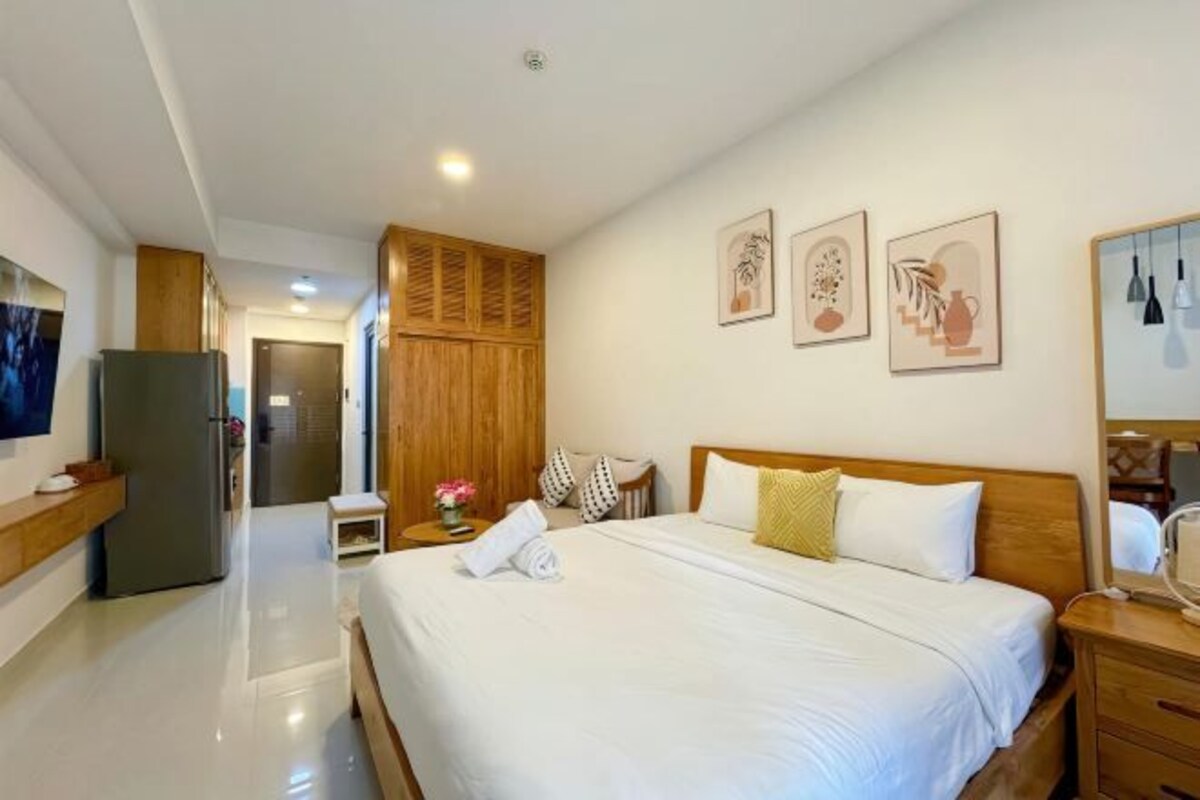 A hotel room with a bed, a wooden wardrobe, a small table with a vase, and a TV on the left wall.