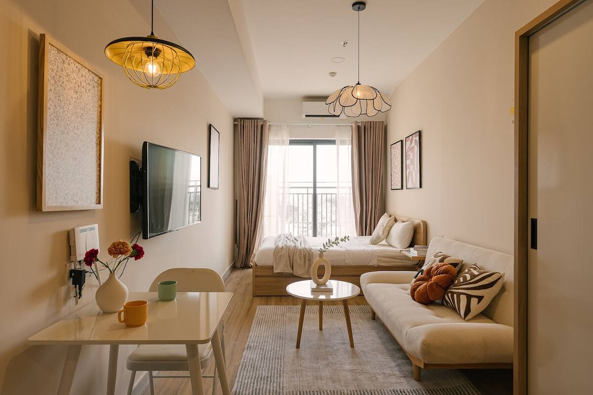 A modern hotel room with a sofa, a dining table, a TV, and a large window with curtains.