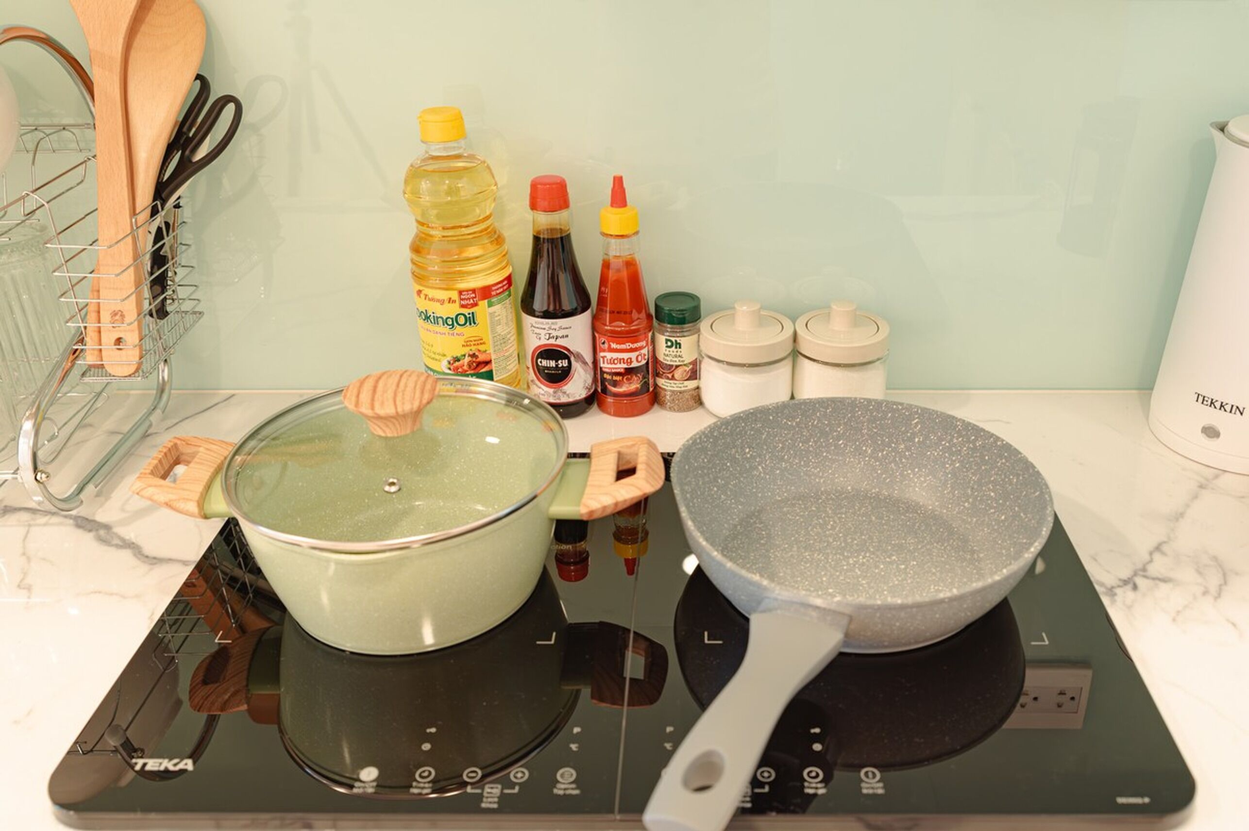 A kitchen with a pot on an induction cooktop, a frying pan, and various cooking ingredients and utensils.