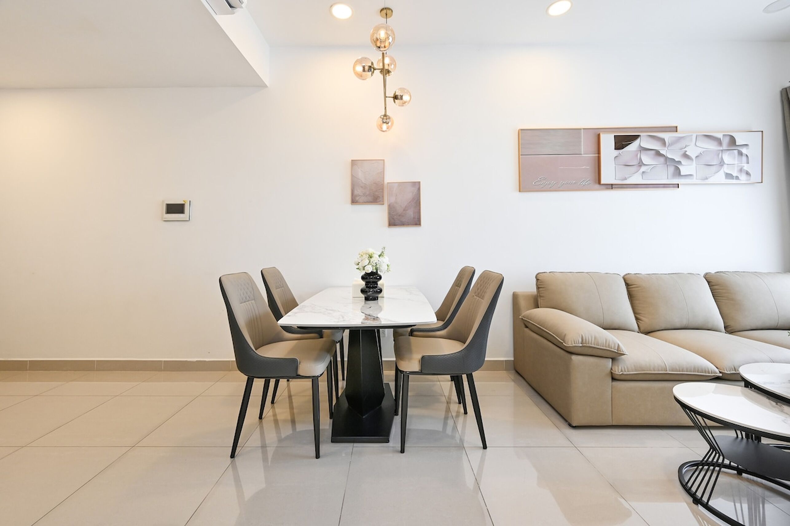 Un comedor moderno con una mesa blanca y cuatro sillas, un sofá color beige y una mesa de centro.