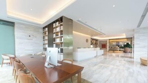 A modern hotel lobby with a wooden reception desk, a large bookshelf, and a marble floor. - JI Hotel (Beijing Shangdi Anningzhuang) (Beijing)