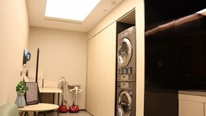 A compact laundry room with a washing machine and dryer, a small table with a plant, and a ceiling light. - JI Hotel (Beijing Shangdi Anningzhuang) (Beijing)