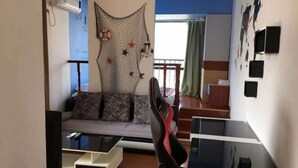 A living room with a sofa, a gaming chair, a coffee table, and a wall-mounted TV. - Hanlin Gangwan Apartment (Zhuhai)