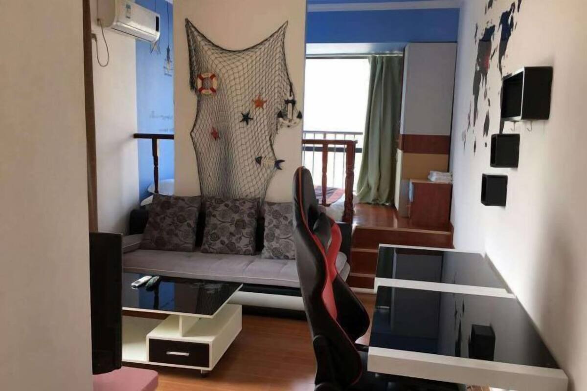 A living room with a sofa, a gaming chair, a coffee table, and a wall-mounted TV.