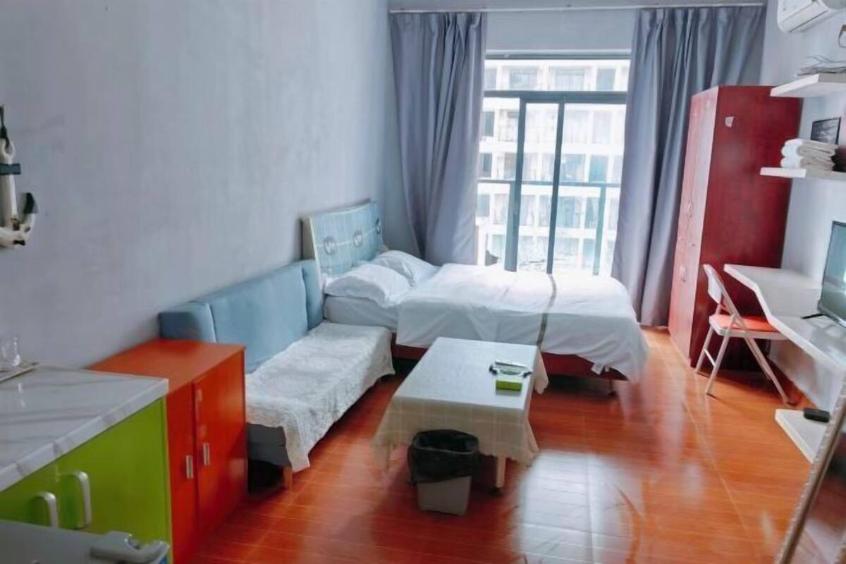 A compact hotel room with a bed, a small table, a desk, and a window with curtains.
