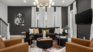 A modern living room with a black sofa, leather armchairs, a round coffee table, and a chandelier.