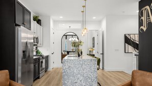 A modern kitchen with stainless steel appliances, a marble island, and a pendant light.