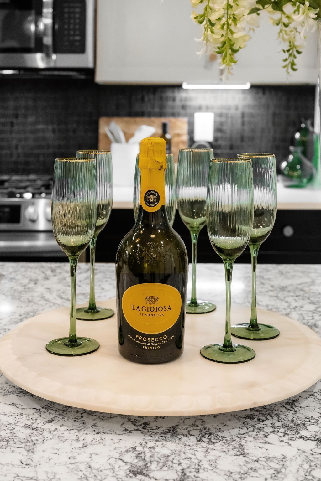 A bottle of Prosecco on a marble countertop with four green wine glasses.