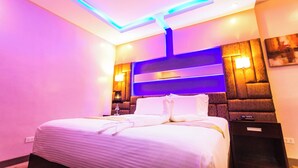 Una habitación de hotel moderna con una cama grande, una mesita de noche e iluminación ambiental.