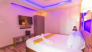 Una habitación de hotel con cama, televisor, armario de madera y mesita de noche.