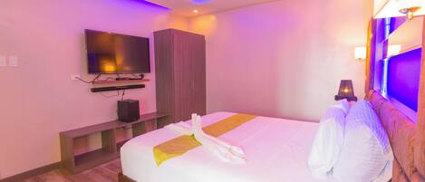 A hotel room with a bed, a TV, a wooden wardrobe, and a bedside table.