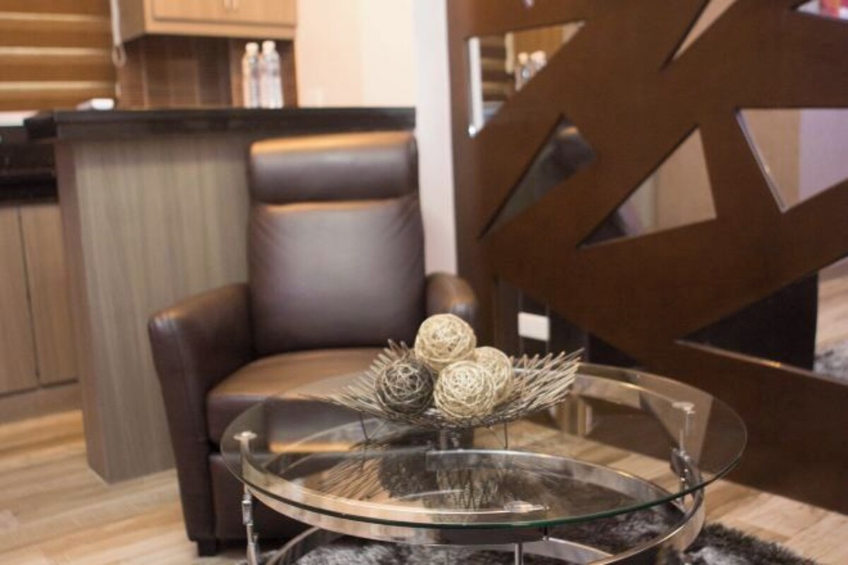 A modern living room with a glass coffee table, a leather sofa, and a decorative vase with spherical ornaments.