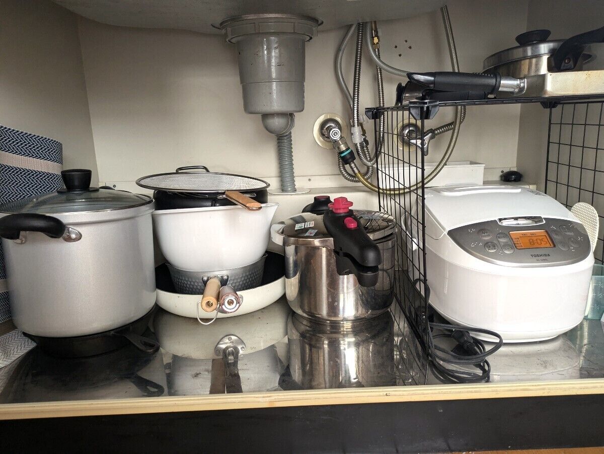 A kitchen counter with various cooking appliances including a rice cooker, pots, and a kettle.