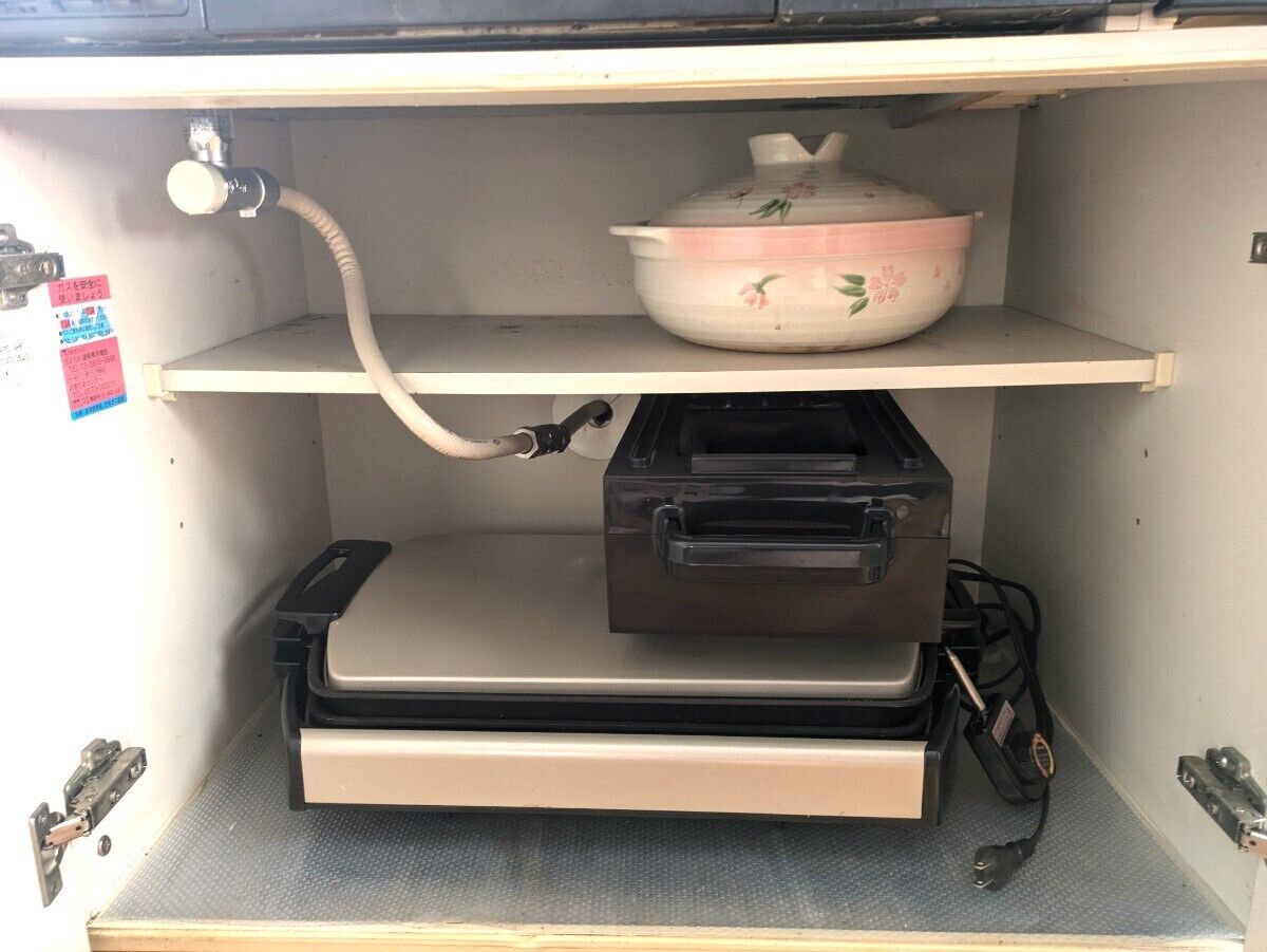 Una cocina con mostrador, pileta y una olla en la estantería.