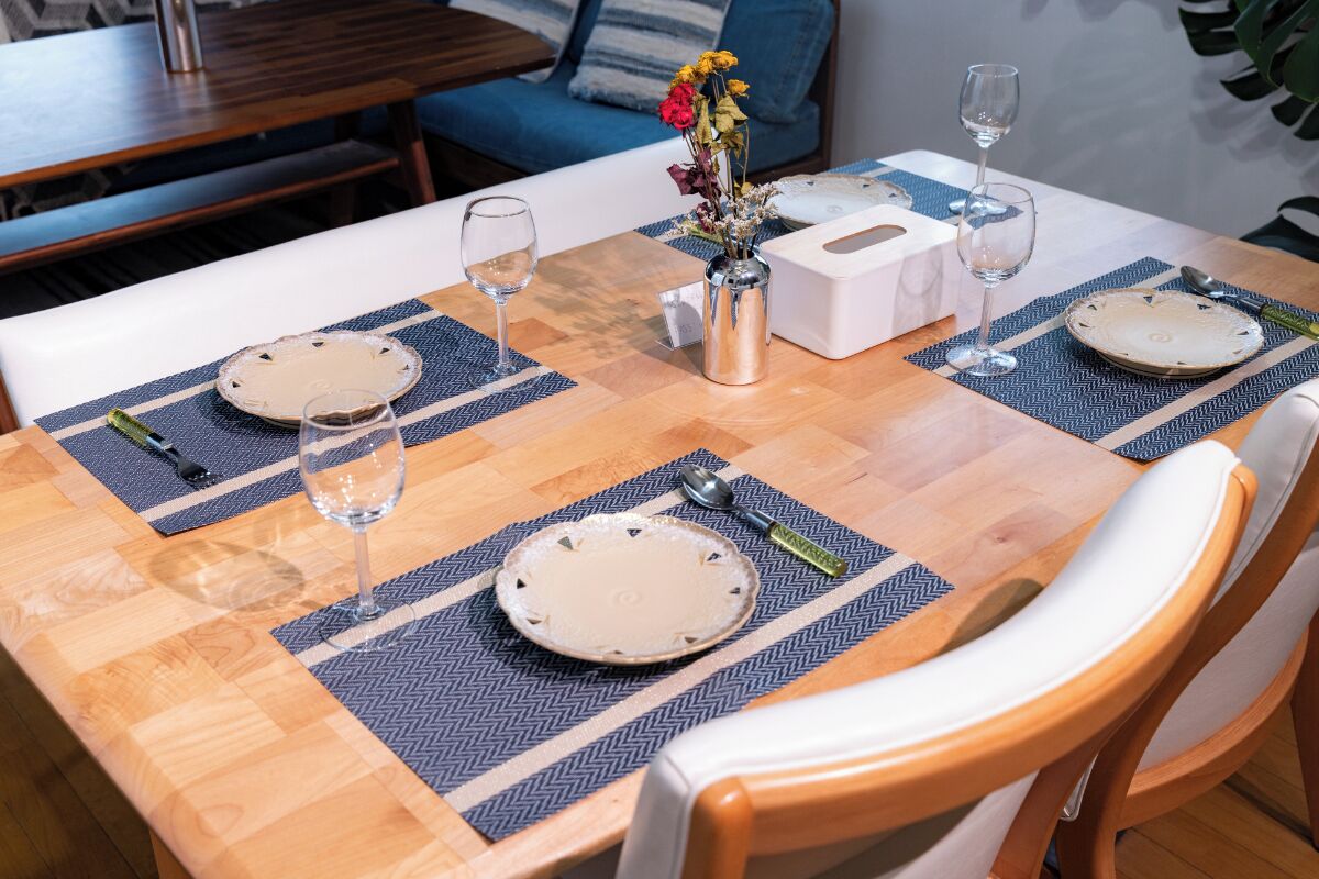 A dining table set with placemats, plates, cutlery, and glasses, with a vase of flowers in the center.