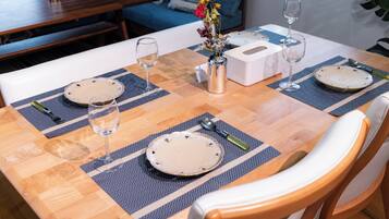 A dining table set with placemats, plates, cutlery, and glasses, with a vase of flowers in the center.