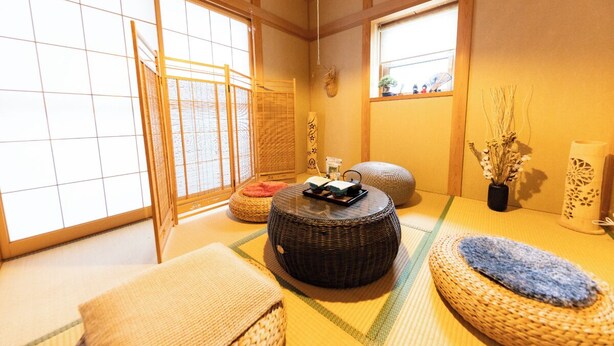 A traditional Japanese room with tatami flooring, a tatami mat table, a woven round stool, and a small wooden shelf with decorative items. - NOT A HOME Kameari Station 5 min. walk Free parking Disney Haneda Airport bus direct 90m2 Tea ceremony experience (葛飾区)