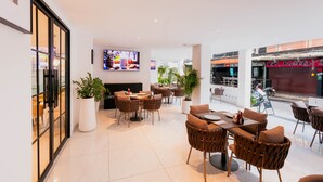 A modern restaurant with indoor seating, a flat-screen TV, and potted plants. - The One Cozy Living (Pattaya)
