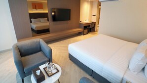 A hotel room with a large bed, a desk with a chair, a flat-screen TV, and an air conditioning unit. - The One Cozy Living (Pattaya)