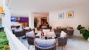 A modern outdoor dining area with wicker chairs and tables, a flat-screen TV, and a neon sign in the background. - The One Cozy Living (Pattaya)