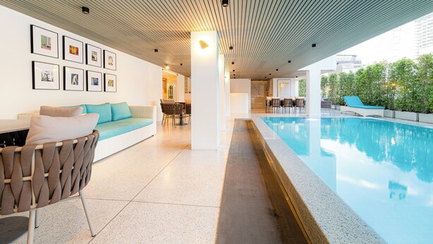 A modern indoor pool area with a seating area and framed artwork on the walls. - The One Cozy Living (Pattaya)
