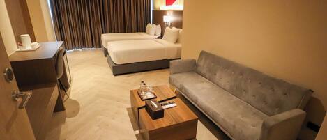 A hotel room with a bed, a sofa, a coffee table, and a desk.