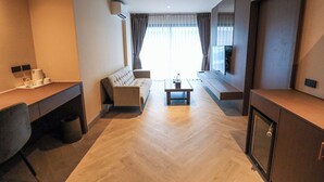 A modern hotel room with a sofa, a dining table, a desk, and a TV. - The One Cozy Living (Pattaya)