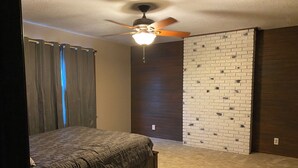 Une chambre à coucher avec un lit, un ventilateur de plafond, un mur décoré d’un motif en briques et un mur recouvert de panneaux en bois.