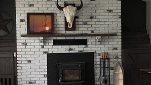 Un salon avec une cheminée en briques, un crâne de taureau accroché au mur, un ventilateur de plafond et un téléviseur fixé au mur.