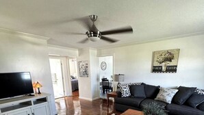 A spacious living room with a dark grey sofa, a wooden coffee table, and a black floral rug. A ceiling fan and a TV on a white cabinet are also visible. - Welcome to The Tennerton House-Charming 2-bedroom with AC and WiFi in Buckhannon (Buckhannon)