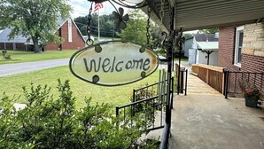 A welcome sign hanging from a building's entrance, surrounded by greenery and a clear sky. - Welcome to The Tennerton House-Charming 2-bedroom with AC and WiFi in Buckhannon (Buckhannon)